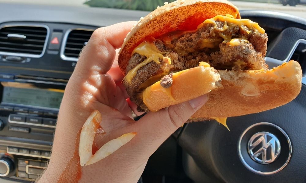 Messy double Quarter Pounder burger held by a driver in car with sauce dripping down arm