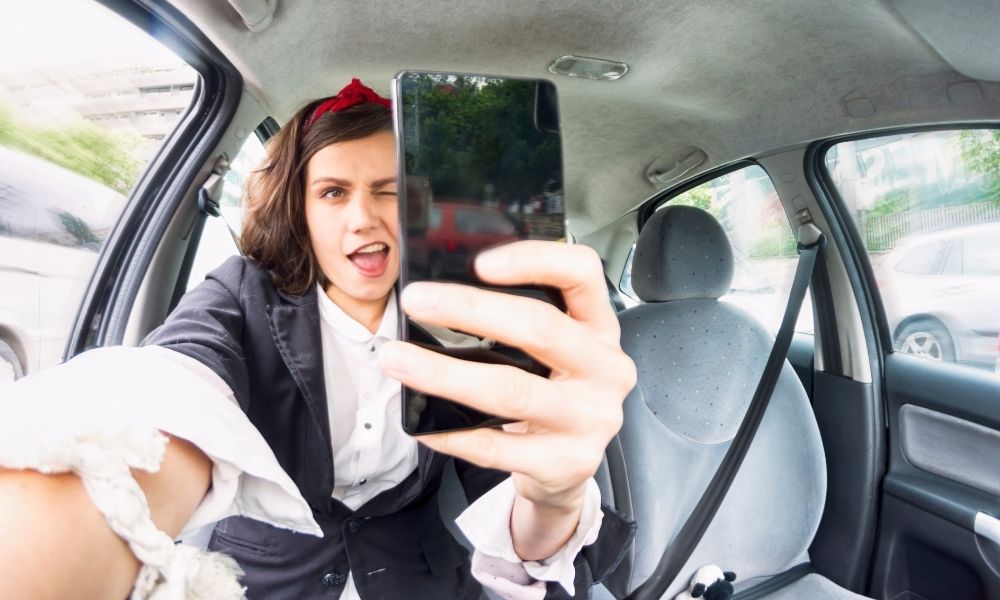 Lady distracted by looking into her phone and taking a selfie while driving a car