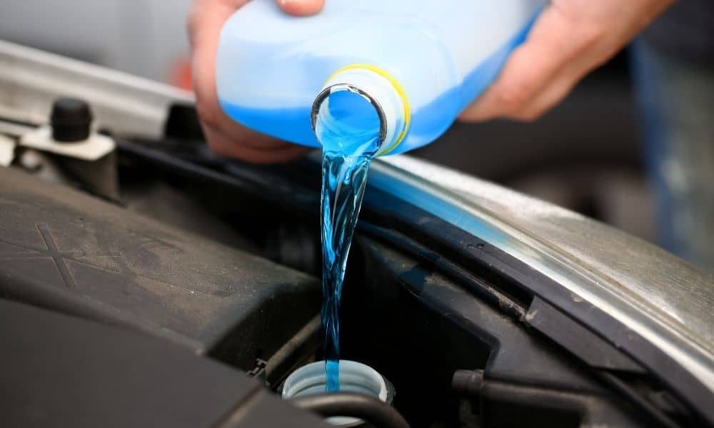 Blue screenwash being poured into car