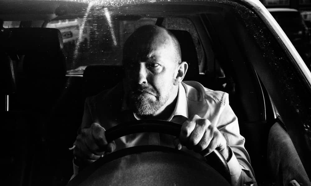 Black and white image of slow driver hunched over steering wheel