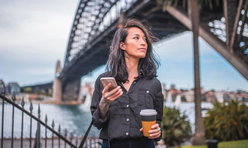 Australian female office worker having coffee while in thought by Sydney Harbour Bridge